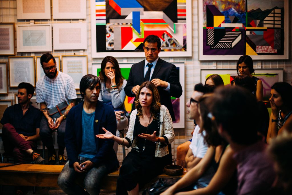 A diverse group of people in a room with colourful artwork on the walls. The people are engaged in a group discussion