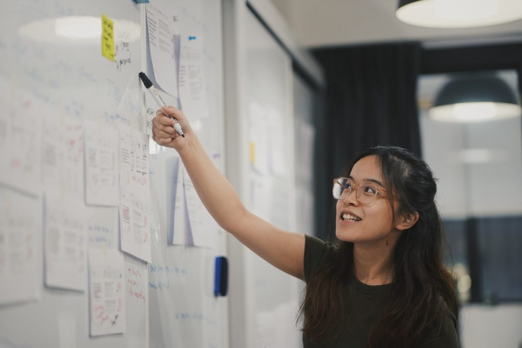 Young Asian woman pointing at a section on a large kanban board