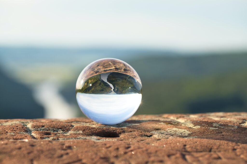 A scenic lens-ball photo, with the backdrop of a river passing through a forest on a sunny day inverted in the glass sphere in the foreground.